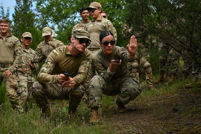 A man and woman in uniform squat next to a bush.