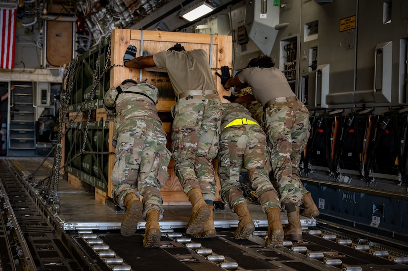 Four service members push cargo up a ramp.