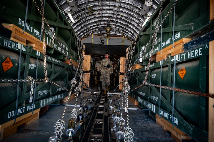 A service member walks amongst cargo and chains in the rear of an aircraft.