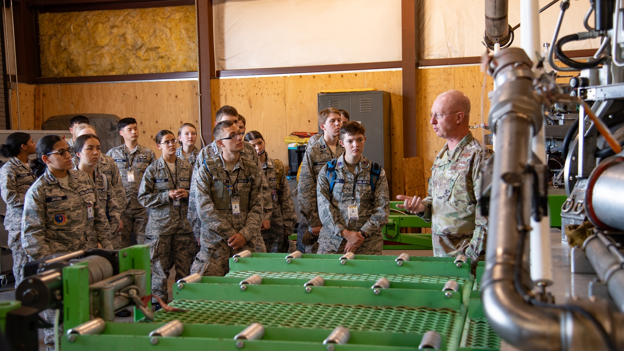 A group of Civil Air Patrol cadets gathered around a piece of equipment listening to an Airman speaking to them.
