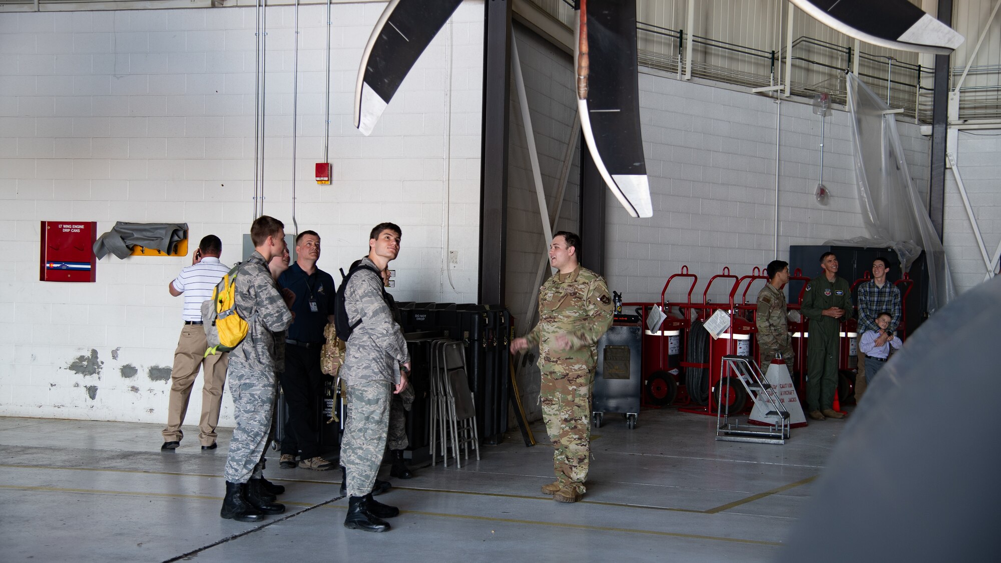 A group in military uniform stands in front of an aircraft propeller.