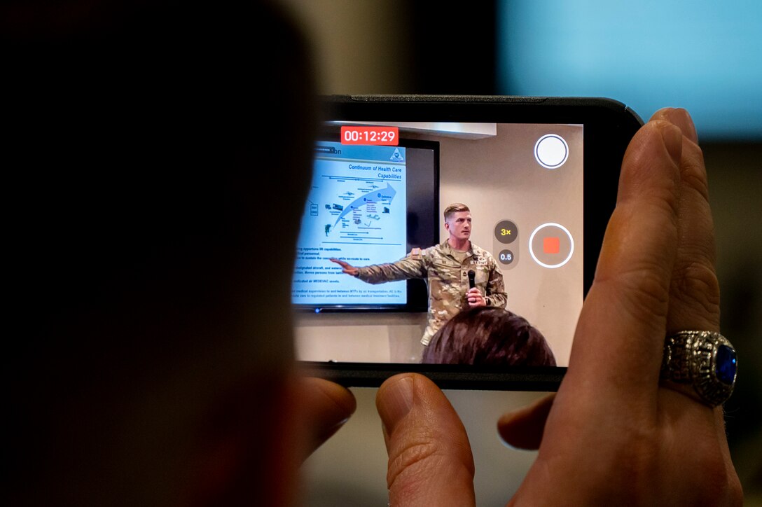 A photo of a person holding a phone recording a presentation.