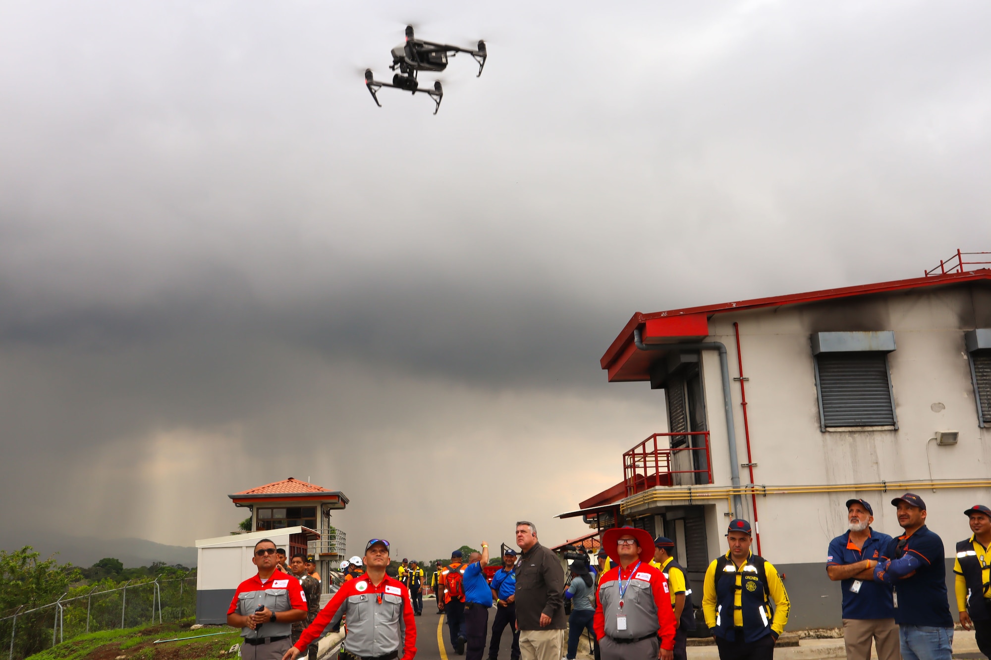 A photo of a firefighter drone in the sky with people looking up at it.