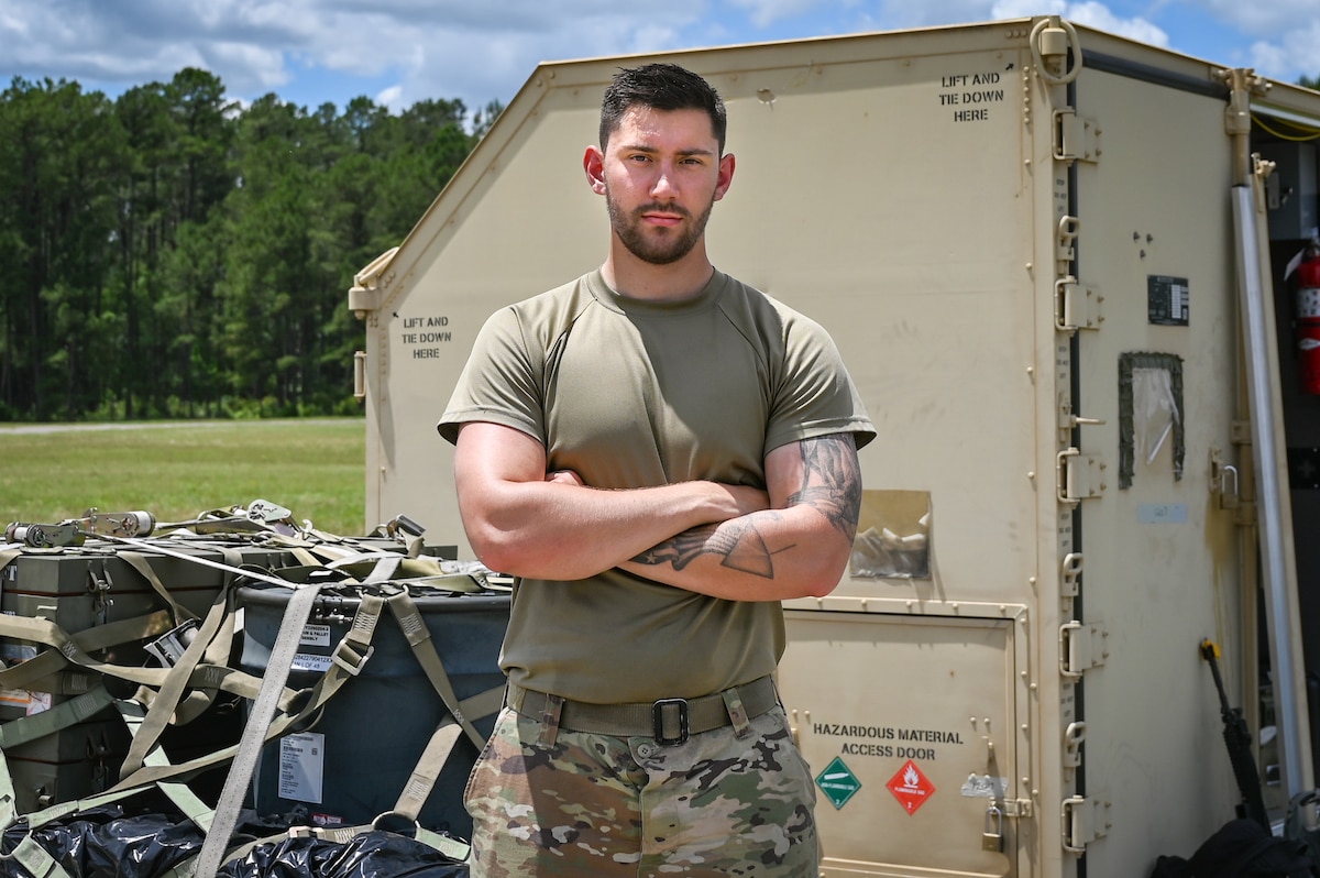 Airman posing with his arm crossed with a big equipment container in the background.