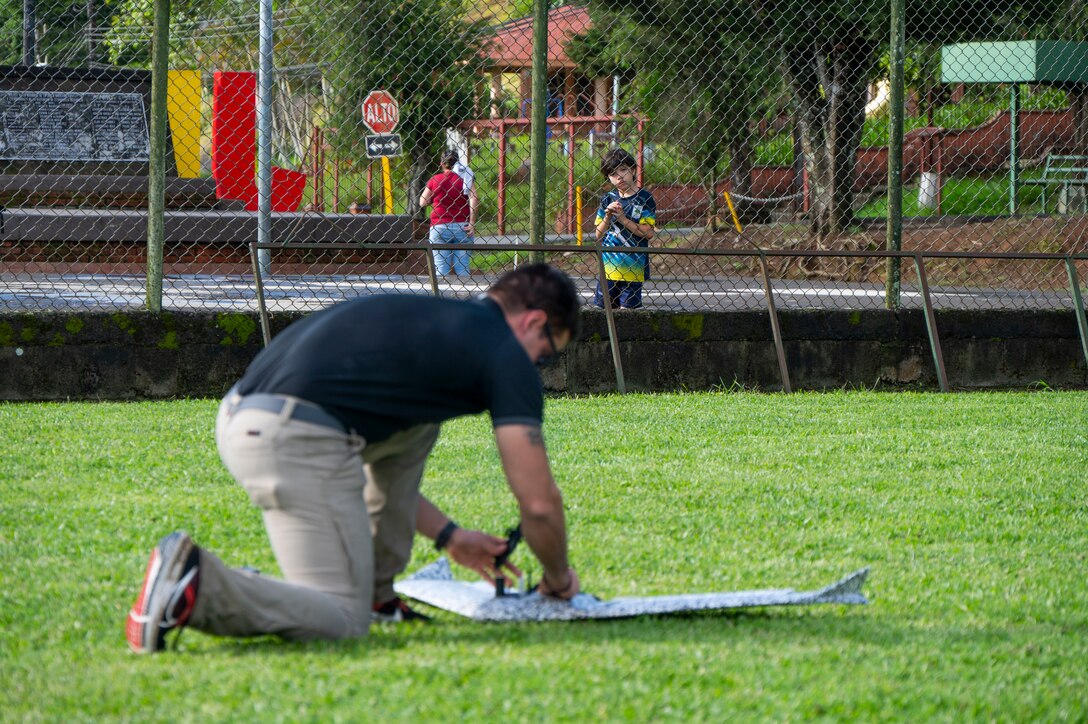 A photo of a person fixing a drone with a little boy watching in the background.
