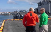 Morten Weesgaard, a Danish harbor pilot, left, and Cmdr. Keith Brooks, a chaplain assigned to the amphibious assault ship USS Wasp (LHD 1), stand on the flight deck as the ship moors to the pier in Skagen, Denmark, June 12, 2024.