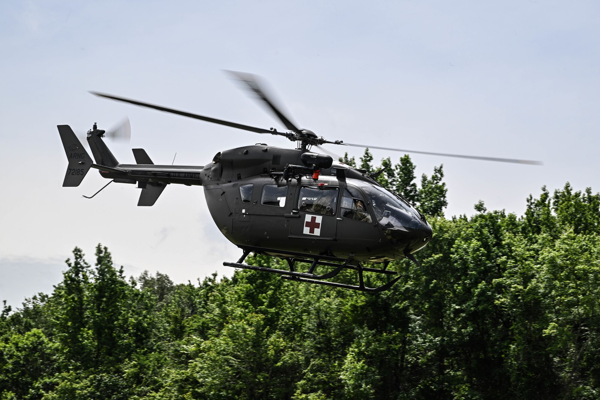 A helicopter flies by a tree line.