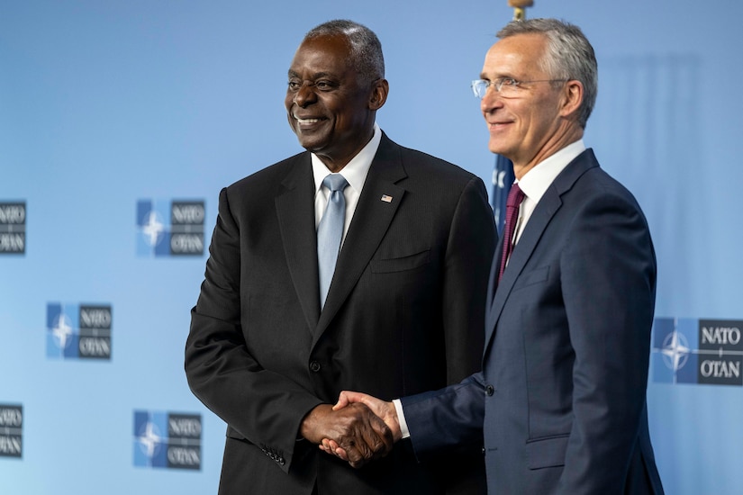 Two people wearing business suits shake hands and smile.