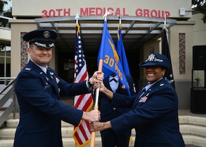 A man in a military uniform hands over a flag to a woman in uniform.