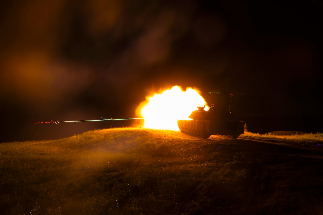 A tank fires, creating a fireball that illuminates a dark field.