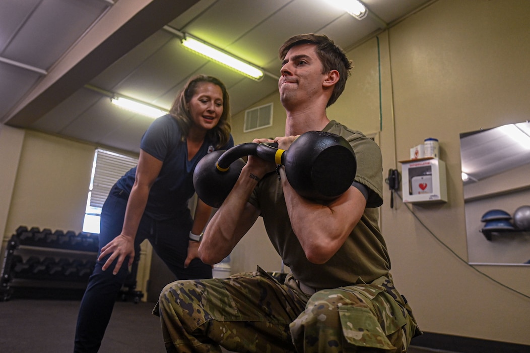 U.S. Air Force Senior Airman Zach Heimbuch, 17th Training Wing public affairs specialist, is coached by Cheri Cotton, Operational Support Team strength and conditioning coach, exercise physiologist, and nutritionist, on how to perform a proper goblet squat with a kettlebell at Goodfellow Air Force Base, Texas, May 30, 2024. OST actively works to transform the culture of each unit, prioritizing physical, mental, and nutritional needs. (U.S. Air Force photo by Airman 1st Class James Salellas)