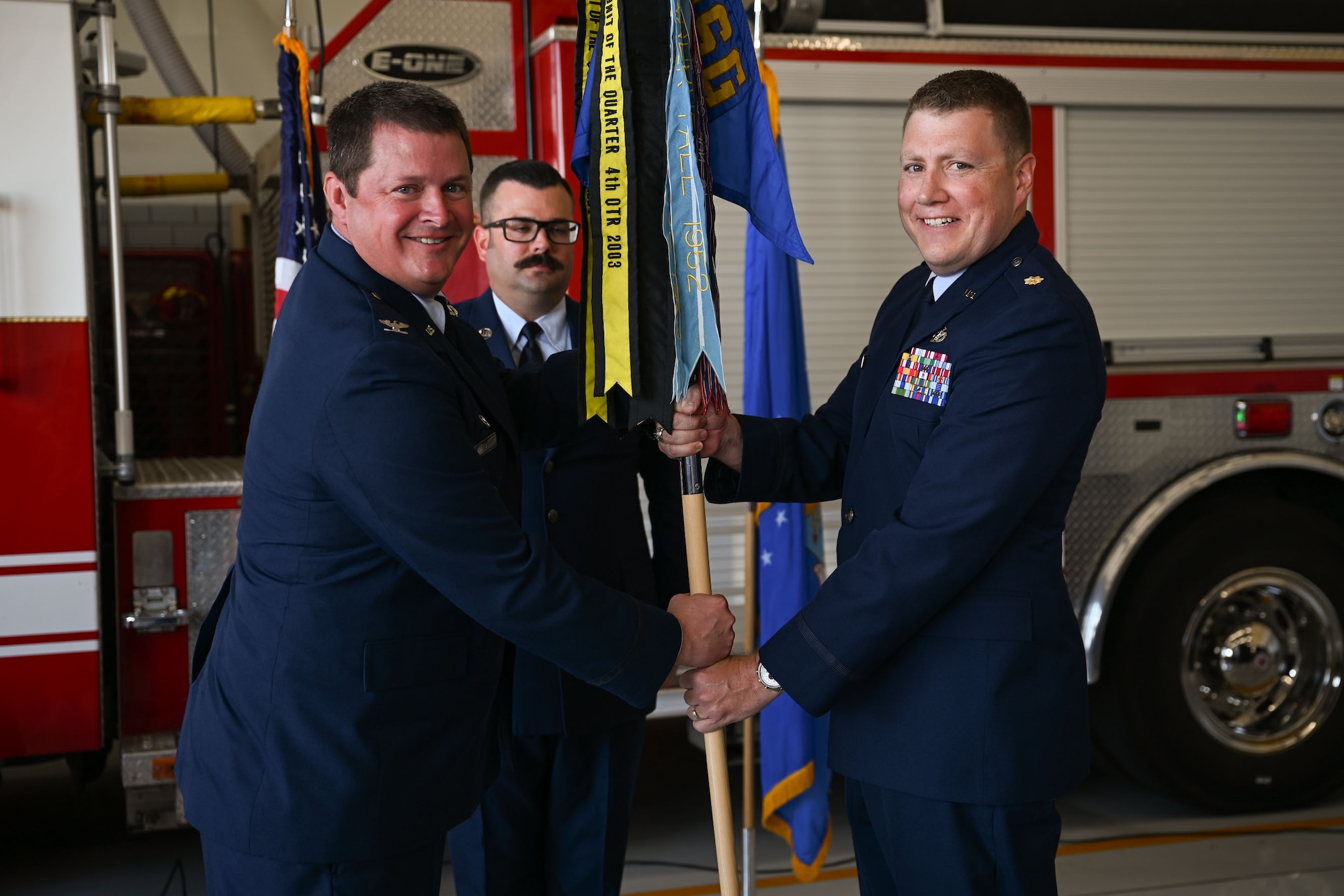 U.S. Air Force Col. Timothy Dalby, 17th Mission Support Group commander, left, passes the guidon to Maj. Levi Beard, incoming 17th Civil Engineering Squadron commander, right, during the 17th CES change of command ceremony at the Goodfellow Fire Department, Goodfellow Air Force Base, Texas, June 13, 2024. The passing of the guidon to Levi signifies him taking command of the 17th CES. (U.S. Air Force photo by Airman 1st Class Evelyn J. D’Errico)
