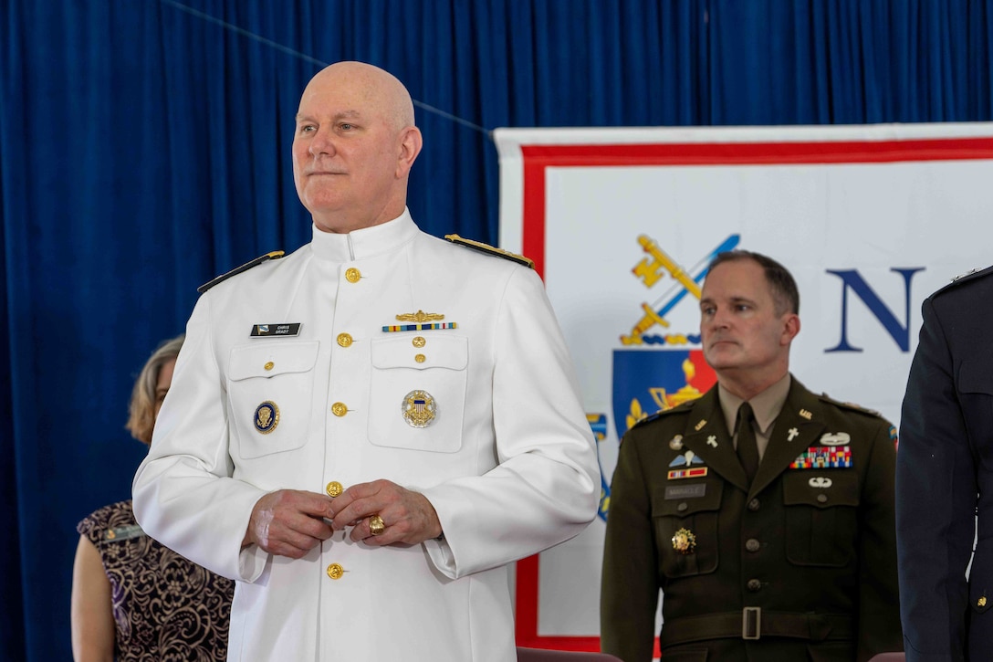 Navy Adm. Christopher W. Grady stands with other service members in front of blue curtain.