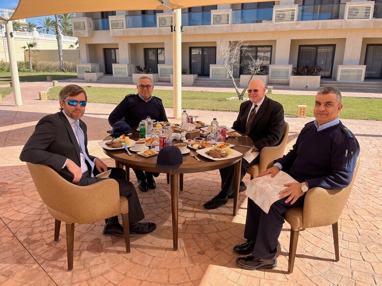 Four men eating outdoors at a round table with an umbrella.