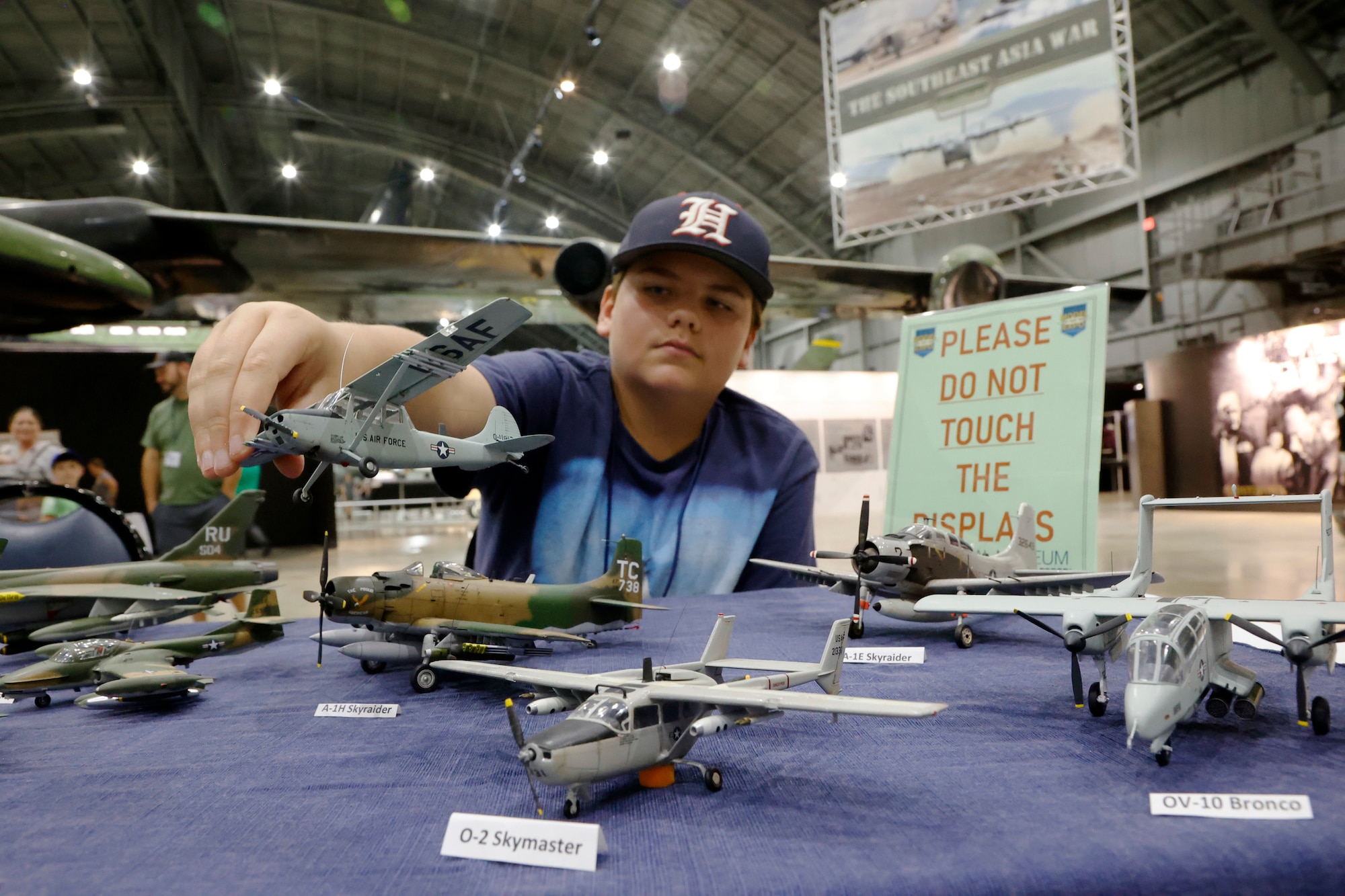 A boy in a blue shirt and hat is placing a model airplane on the table.