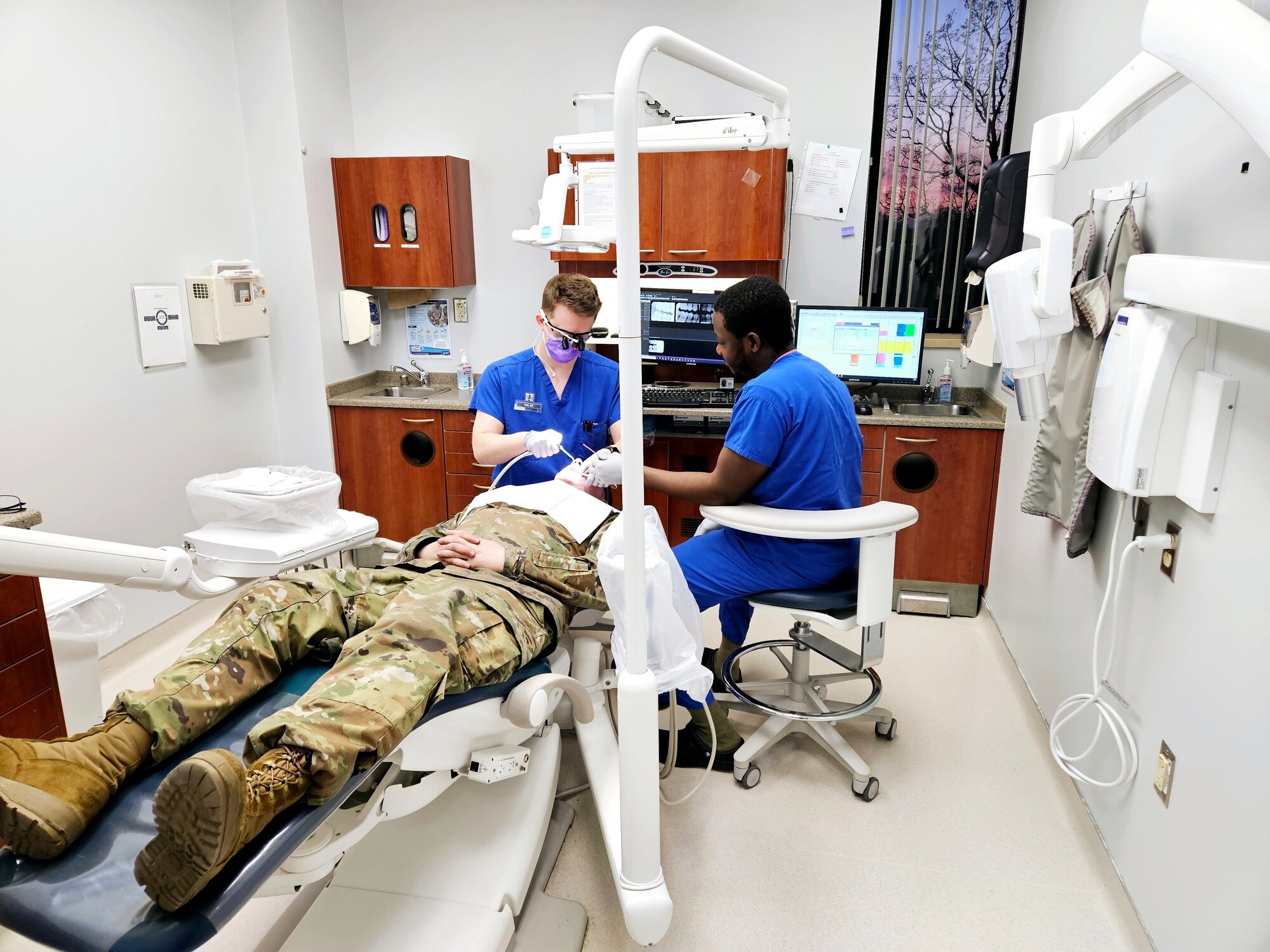 Two dental workers provide dental care to a patient in uniform.