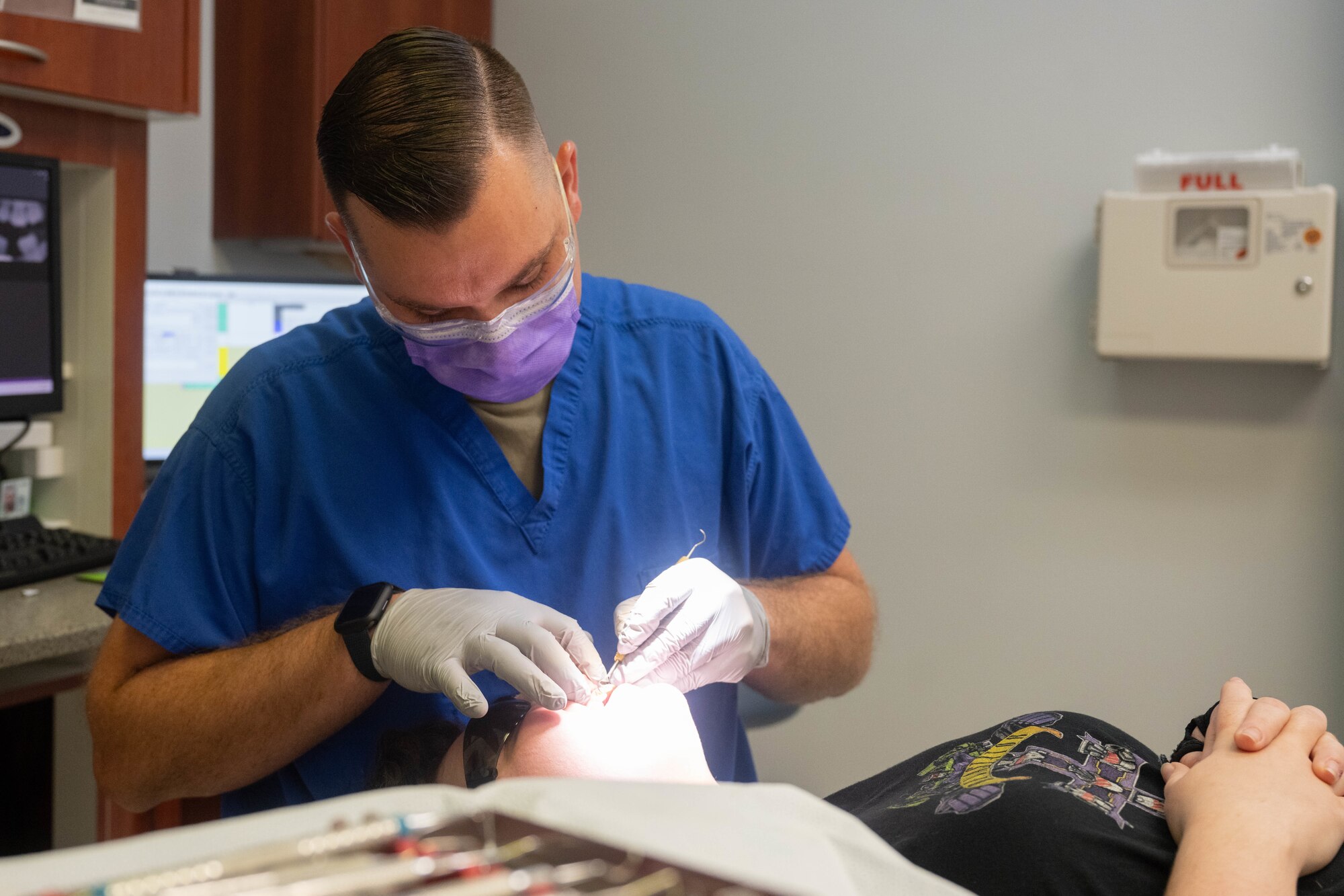 A man wearing scrubs provides dental care to a patient.