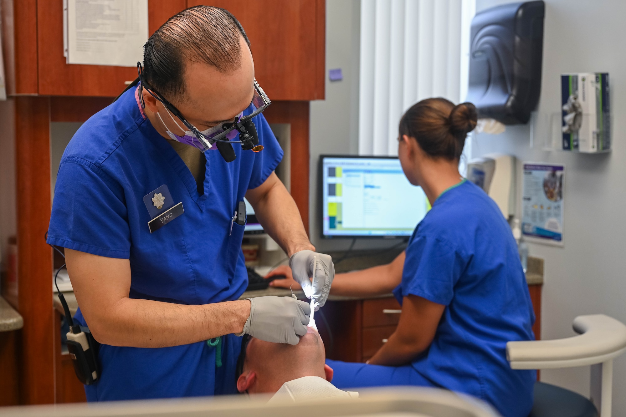 A man wearing scrubs provides dental care to a patient.