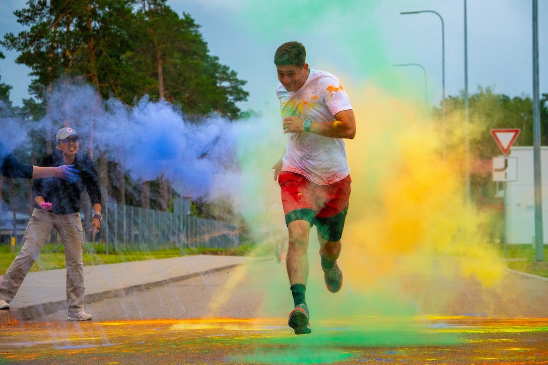 A runner goes through yellow, green and blue clouds  on a road where people are tossing colored powder.