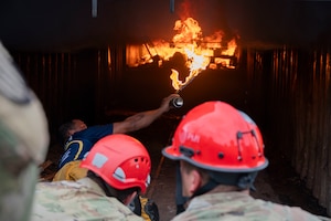 A photo of a person spraying fire into a storage container while others watch.