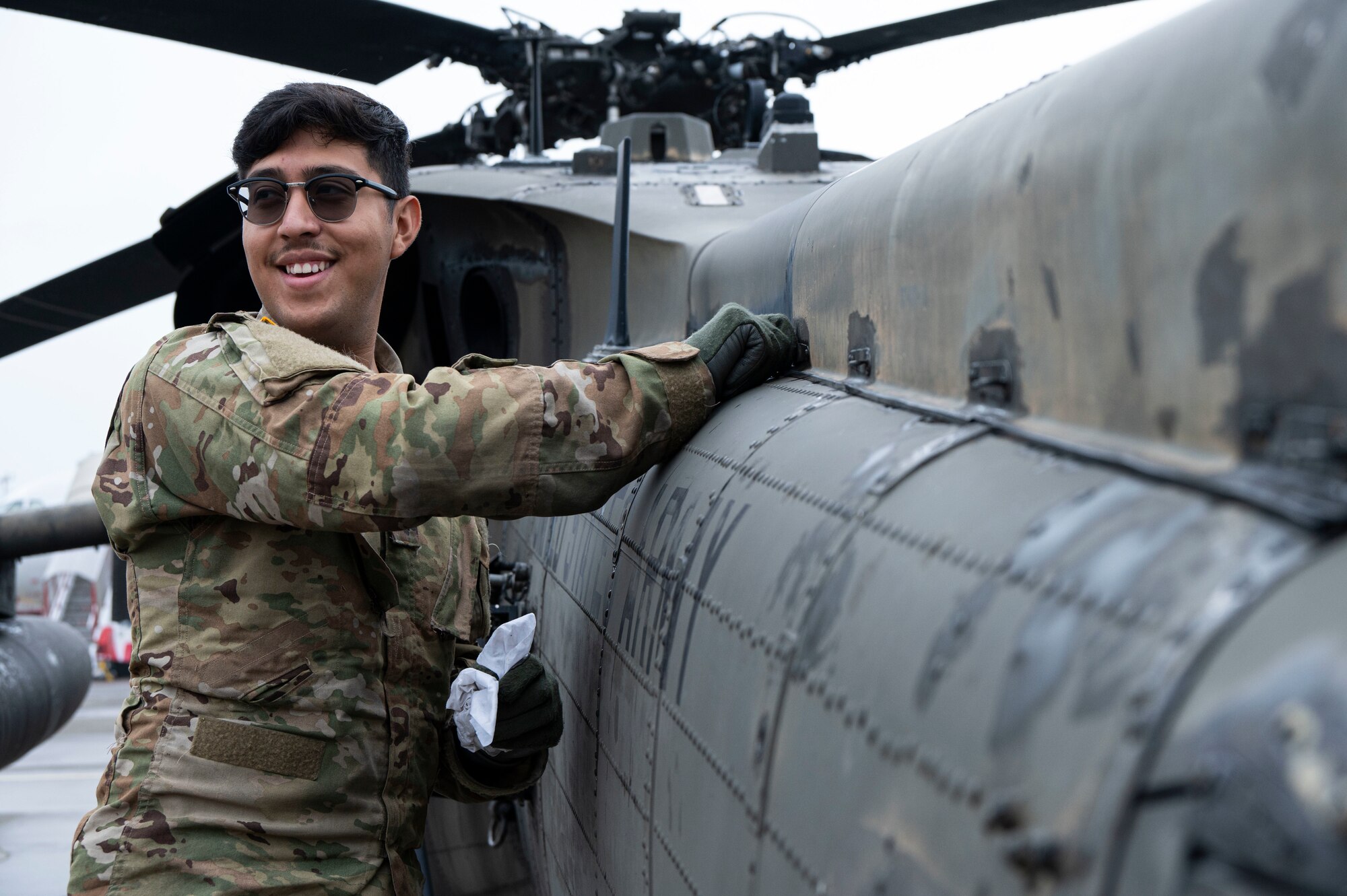 A photo of a person smiling while inspecting a helicopter.