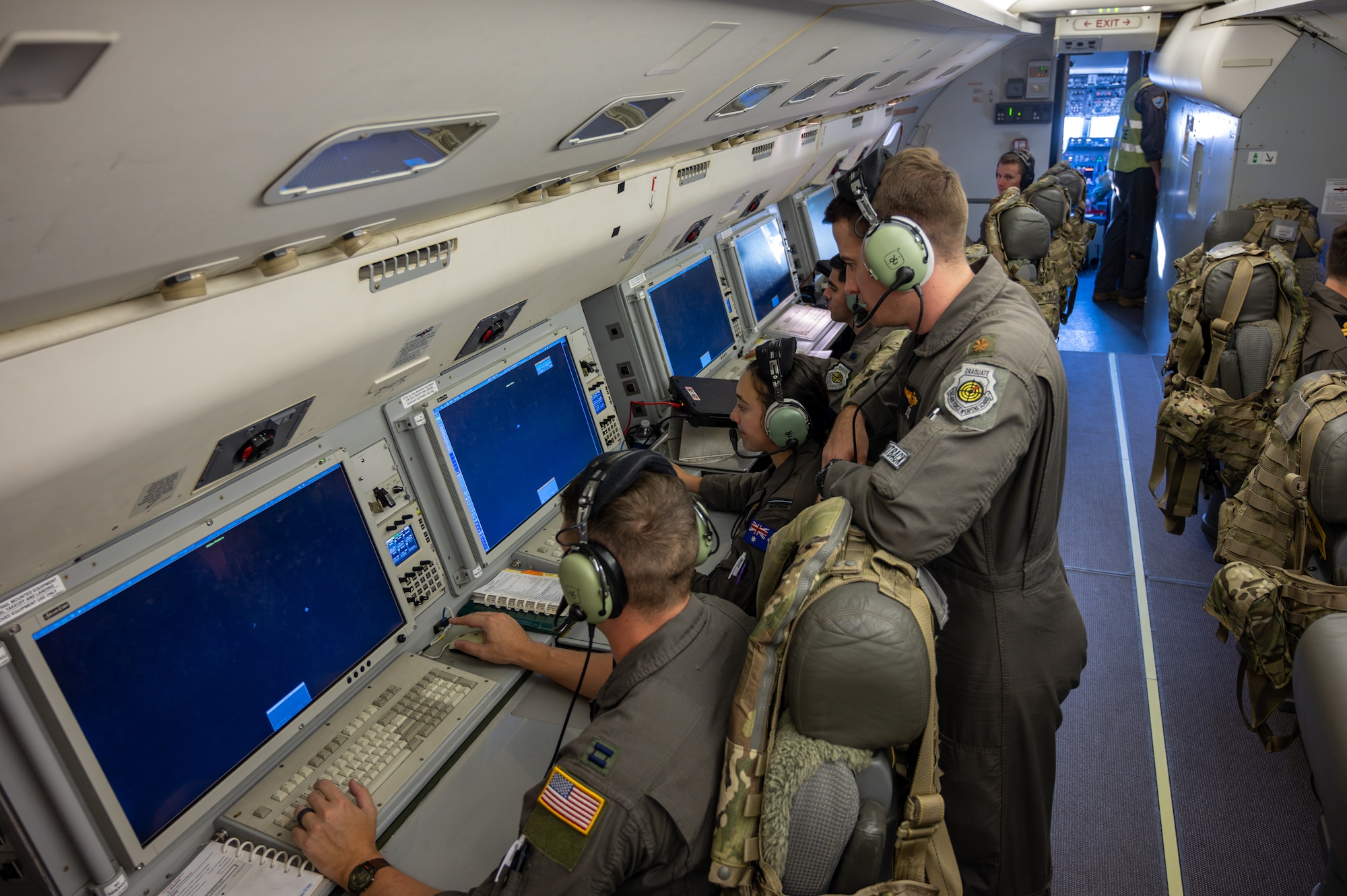 Four people sit at the on-board mission console while another man stands behind them.