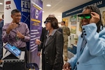 A person speaks as two others wear technical glasses in front of a floor display.