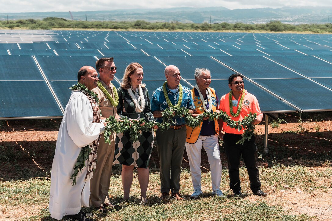 People wearing leis and jointly holding a long garland stand for a photo in front of a solar farm.