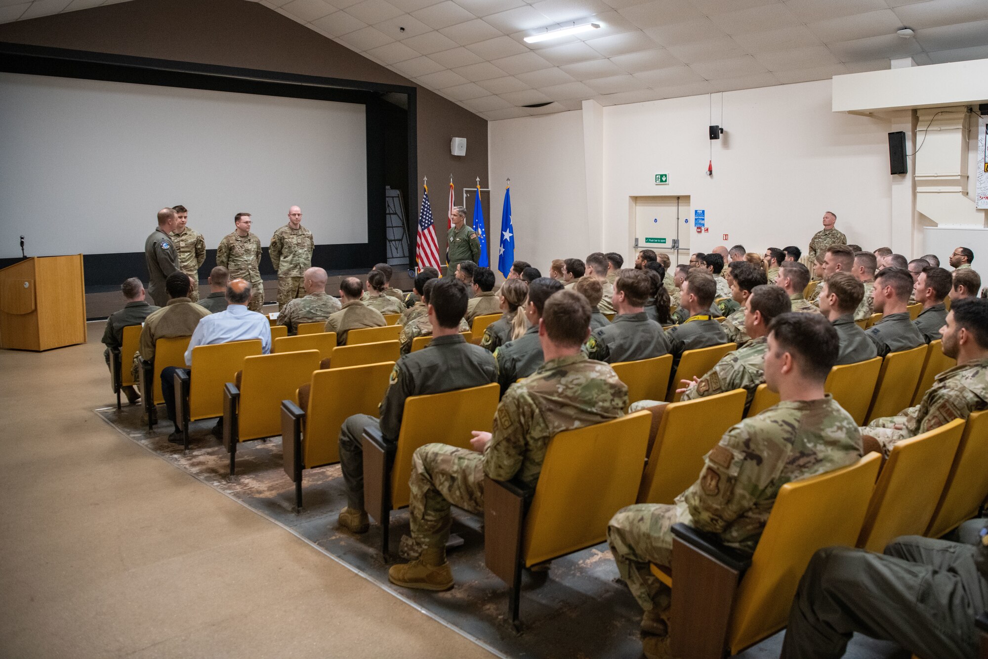 A room full of people sit while watching Airmen being recognized