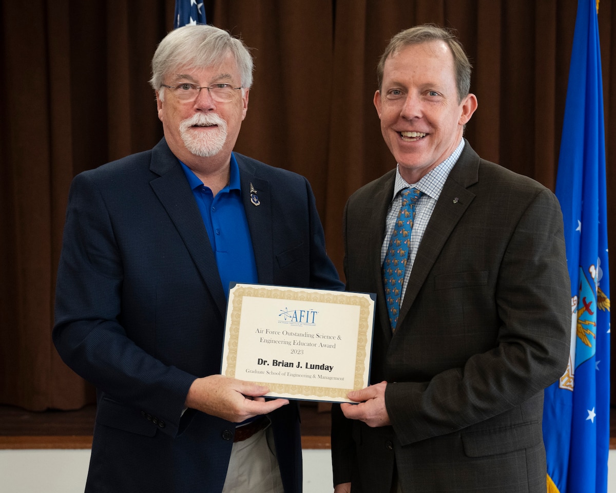 Dr. Jones presents certificate to Dr. Lunday in front of the Air Force flag.