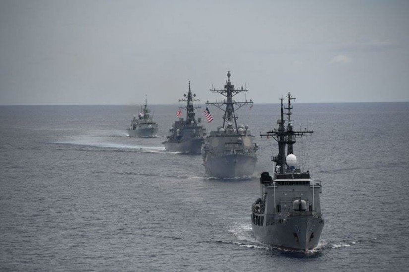 Four ships sail in a row in open water.