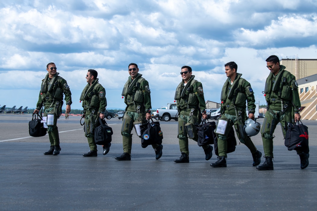 5 pilots from the Indian Air Force walk across the flightline in a line each with their flight helmet bags in hand.