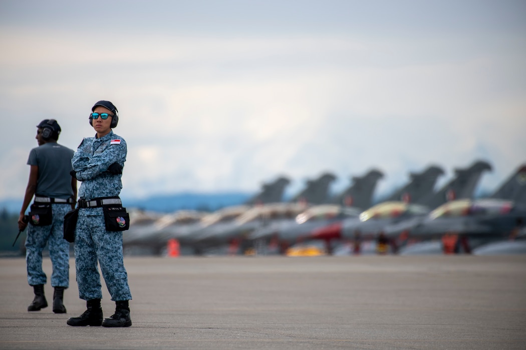 Two maintainer from the Republic of Singapore stand on the flightline in front of jets.
