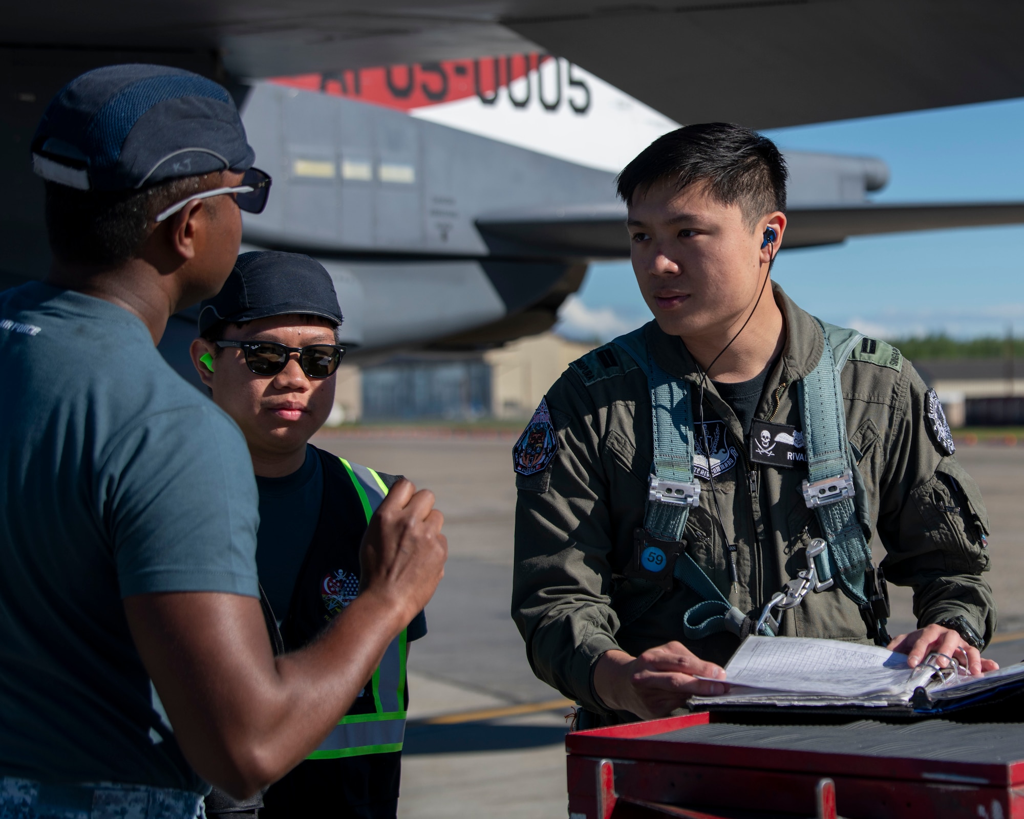 A pilot fills out papers while listening to two other maintainers.