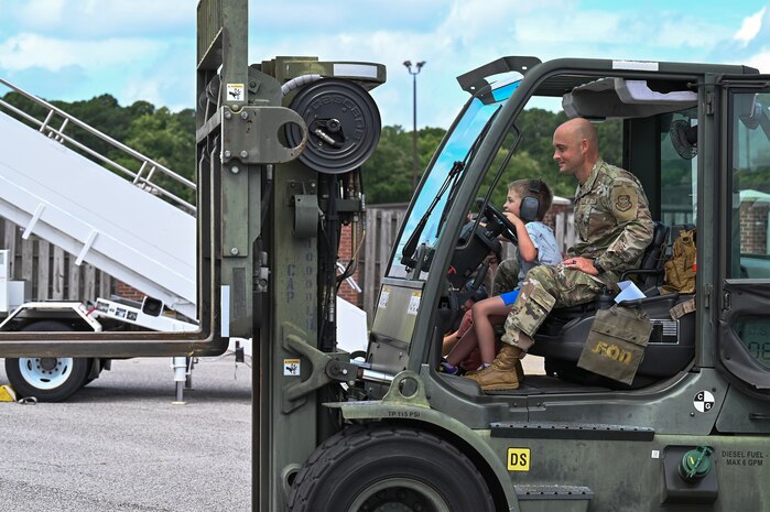 Airman and his son operate equipment during bring your family to work day.