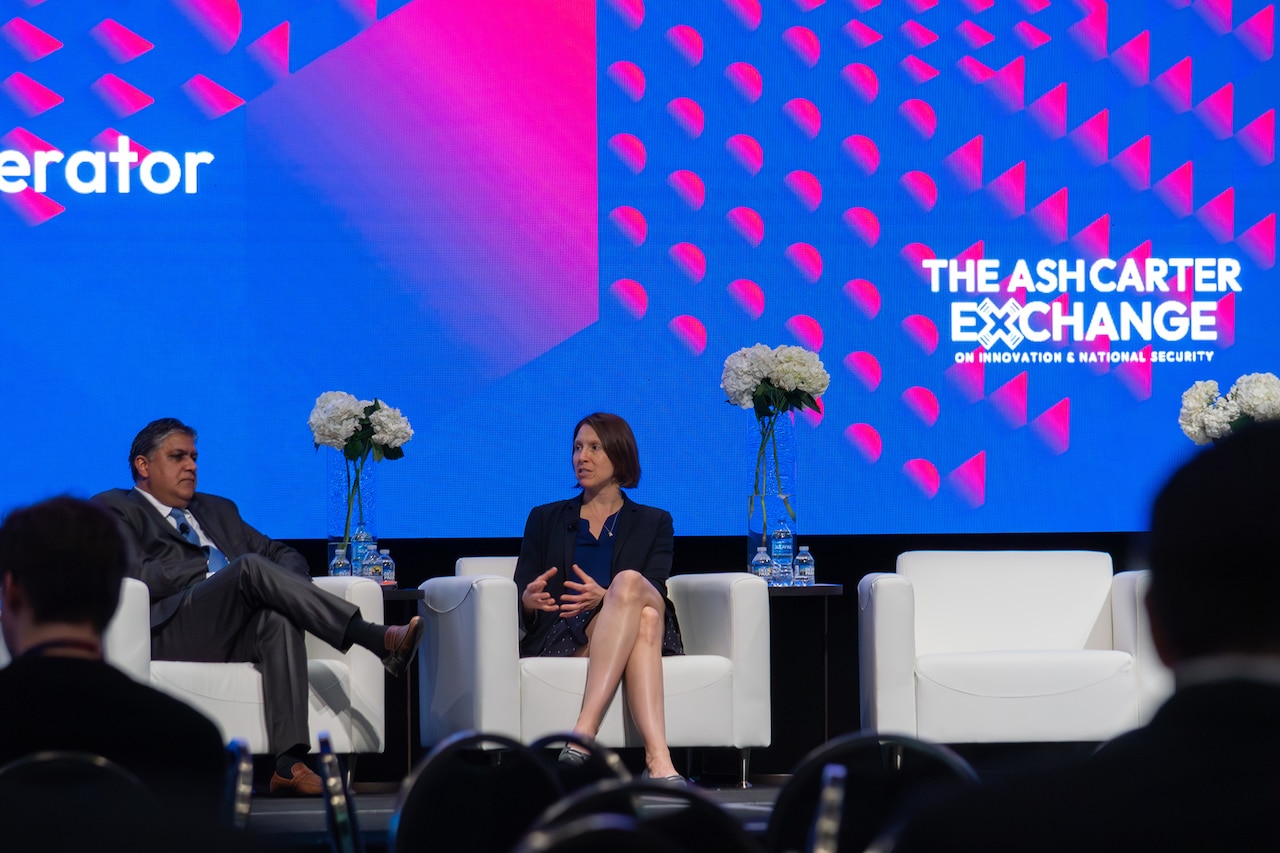 Two people in business attire are seated on a stage.