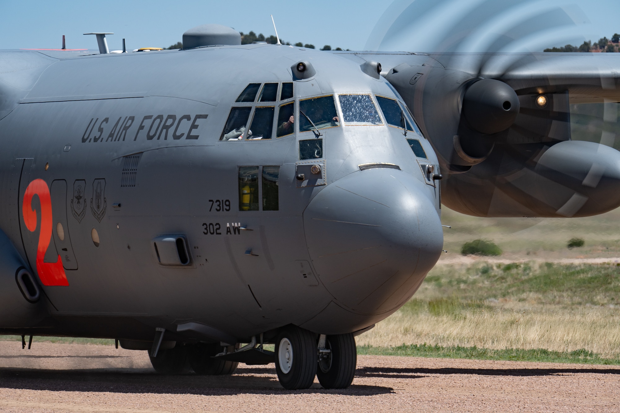 A military aircraft taxis on a dirt airstrip.