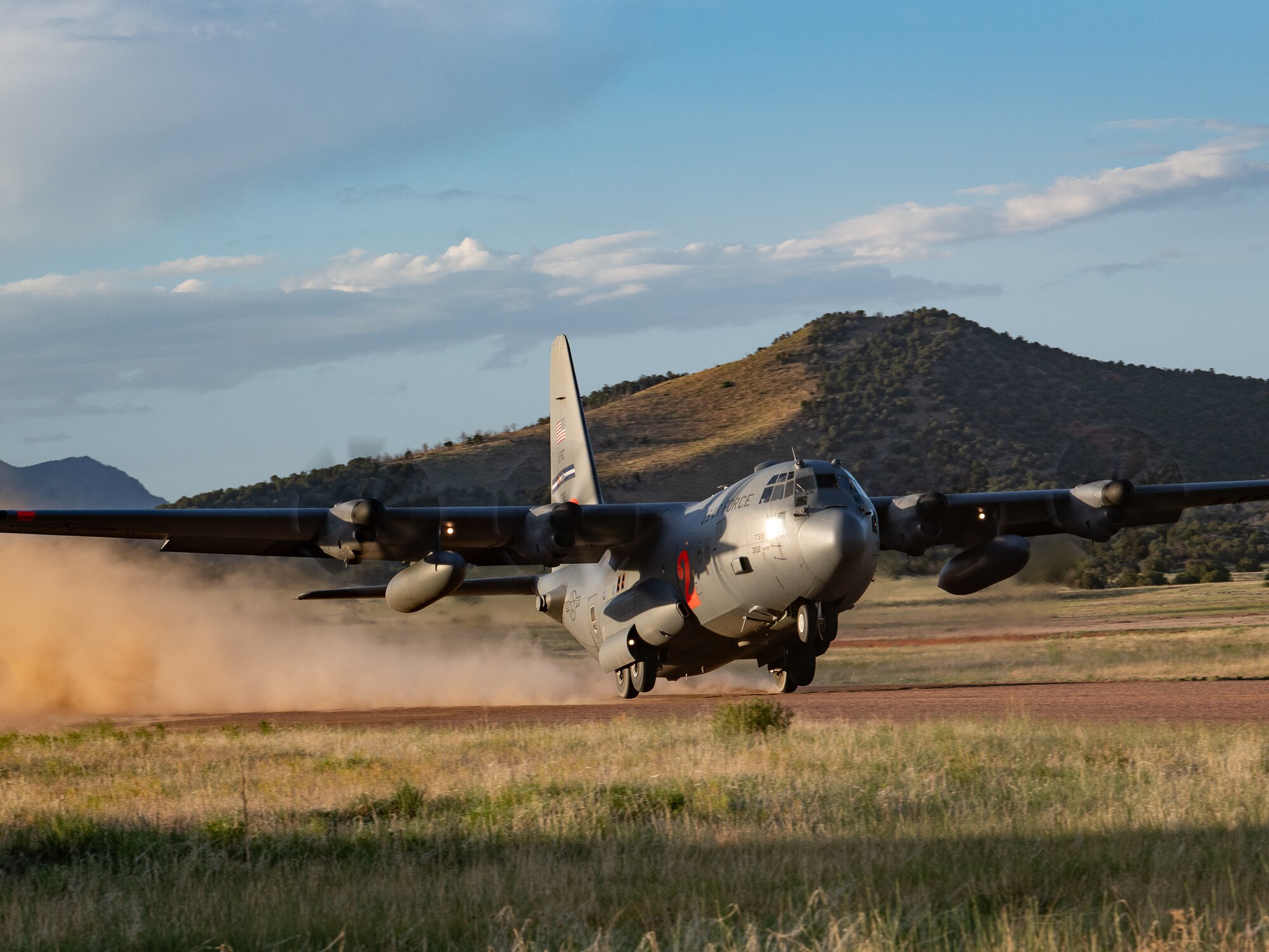 A military cargo aircraft takes off at a dirt landing strip kicking up dust as it aims skyward.