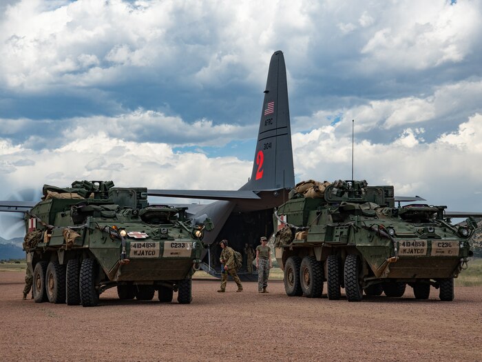 Two military medical evacuation vehicles parked in front of a military aircraft on a dirt airstrip.