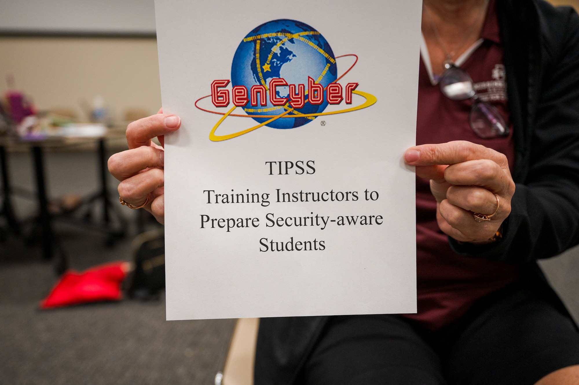 A GenCyber graphic is held up by Shelly Hollis, Mississippi State University Center for Cyber Education director, during the MSU GenCyber camp for local K-12 teachers at Keesler Air Force Base, Mississippi, June 7, 2024.