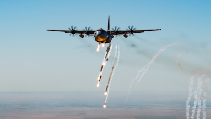 A military aircraft dispenses chaff and flares underneath it in flight.