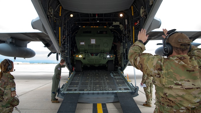 A truck being marshalled into the back of a military cargo aircraft.