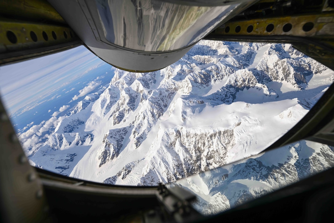 Snow covered mountains are seen from a large aircraft flying above.