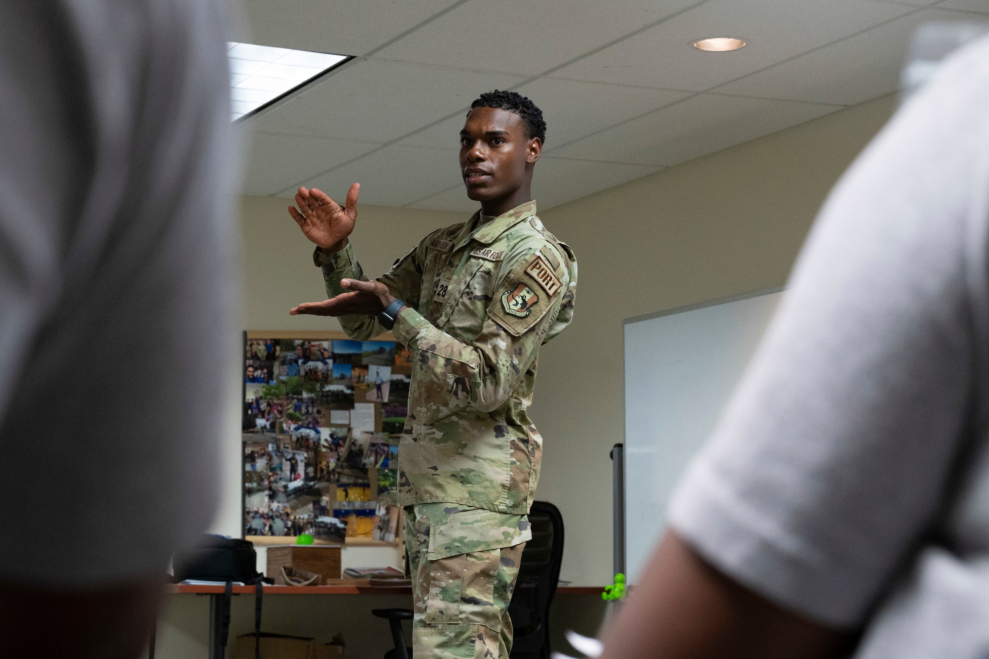 A man gestures while speaking to a classroom of people.
