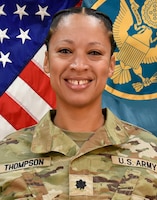 Woman in Army uniform standing in front of two flags