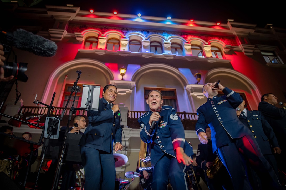 U.S. and Peruvian air force band members perform on stage under red and blue spotlights.