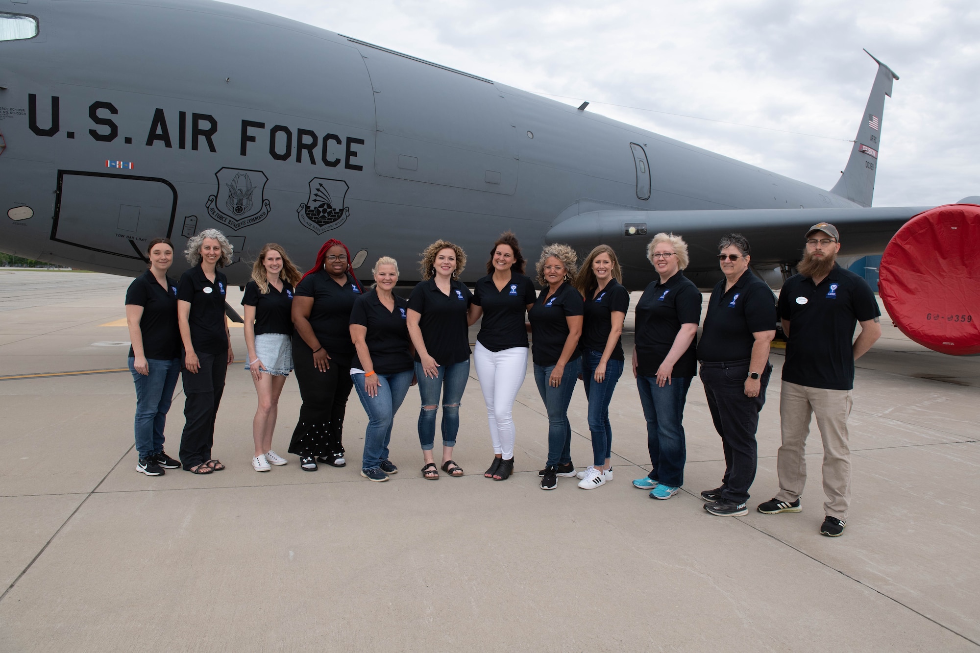 A group of civilians pose for a photo in front of a static KC-135R Stratotanker. All are dressed in black polo shirts.