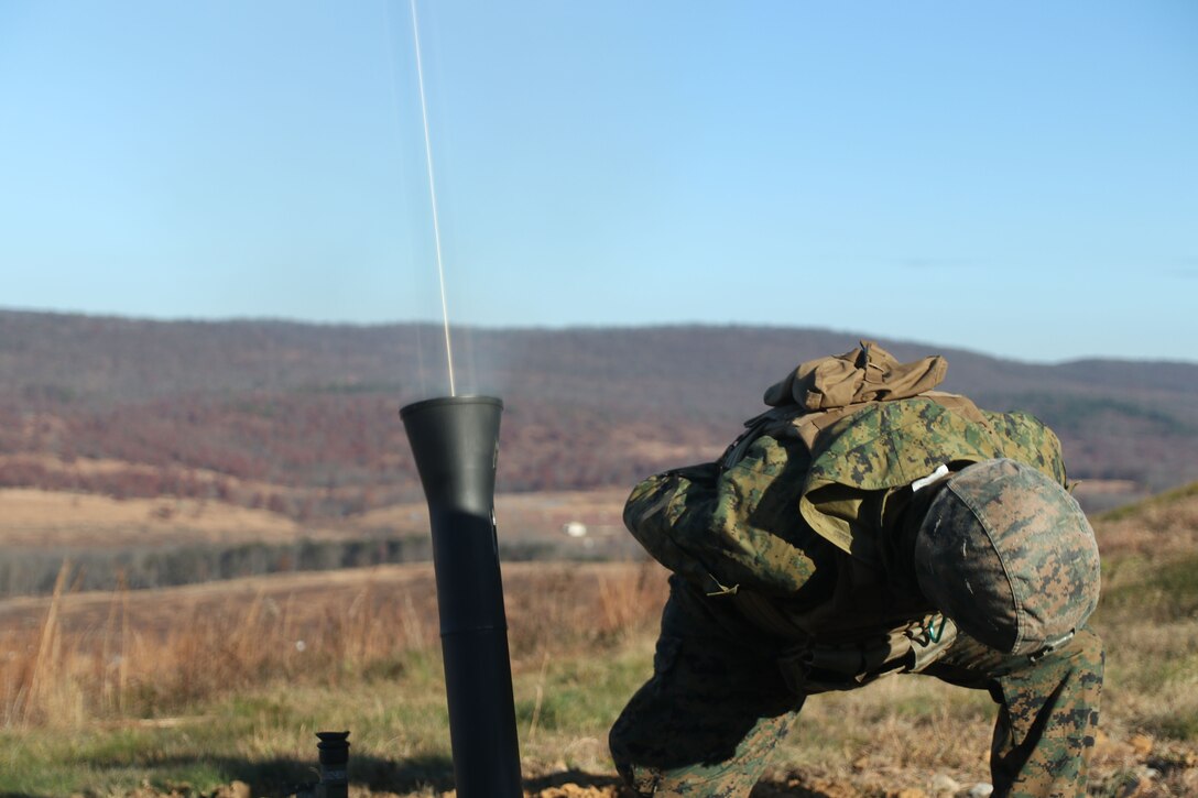 A Marine crouches down and turns away from a tube as it emits a beam of light.