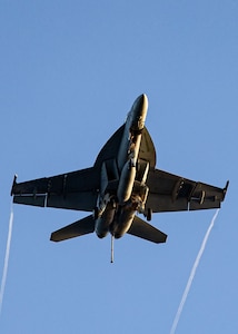 F/A 18 aircraft seen from below climbs into a blue sky.