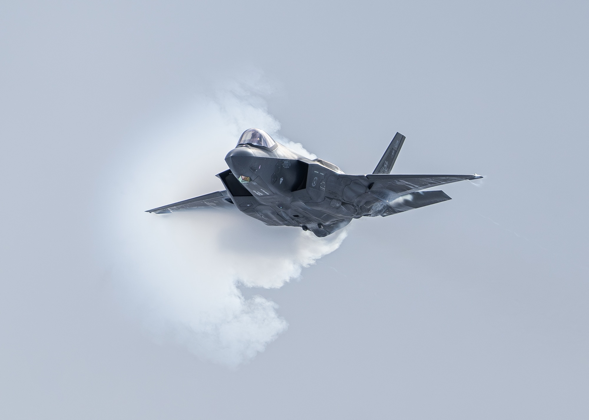 An F-35a dlies through the air with a vapor cloud surrounding.